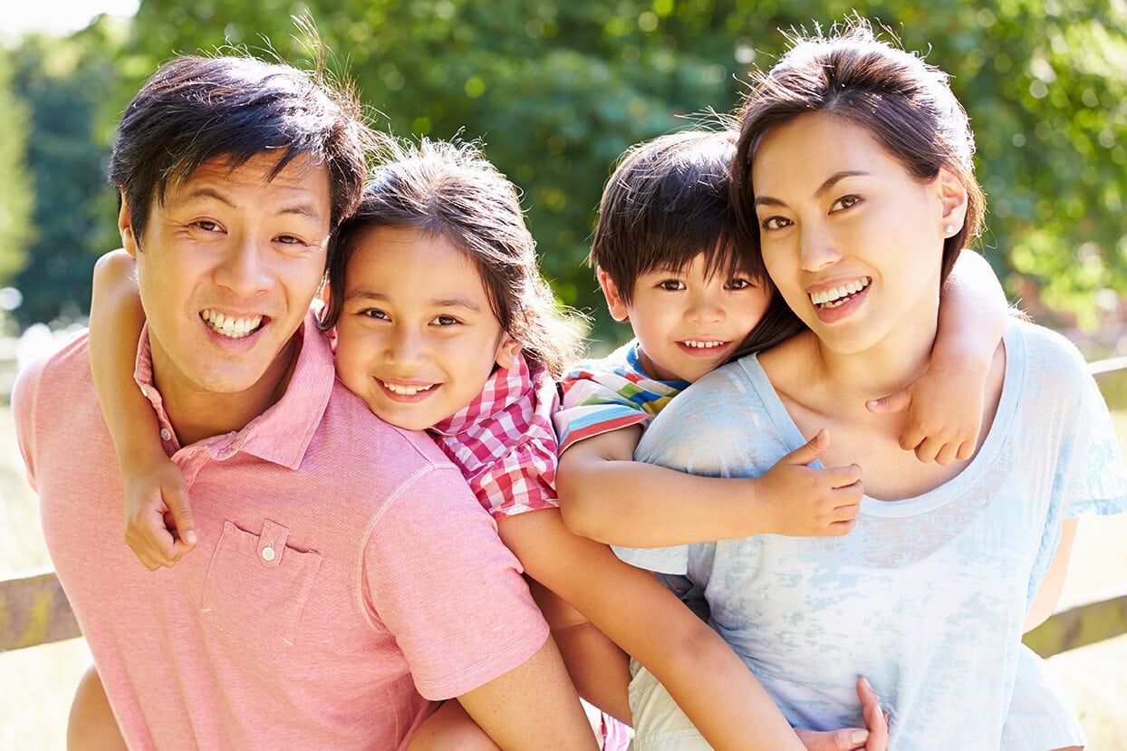 A smiling family outdoors on a sunny day.